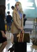 Elle Fanning sports Gucci glasses paired with a tan blazer, blue shirt, jeans and brown boots as she arrives at the CDG Airport in Paris, France