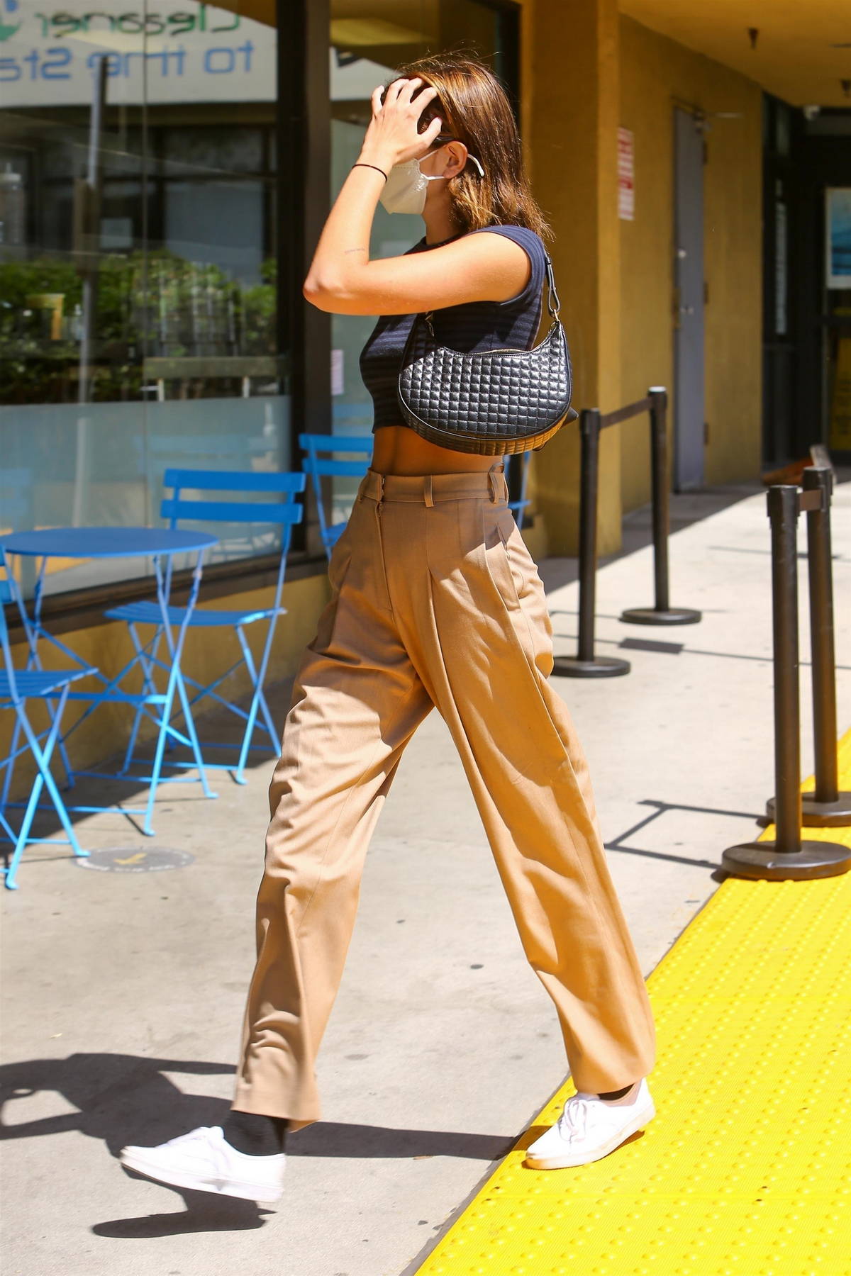 kaia gerber wears a black crop top and brown pleated trousers